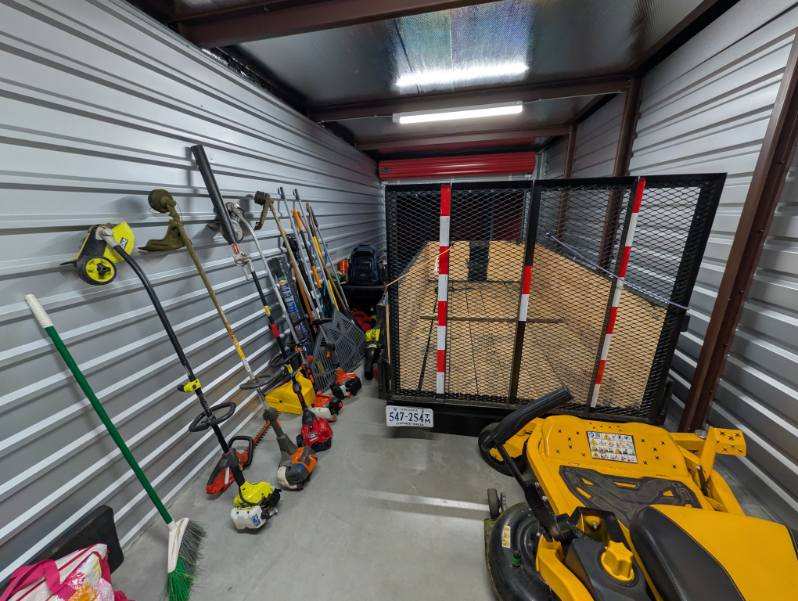 Landscaping equipment including trimmers, trailer, and riding mower in storage