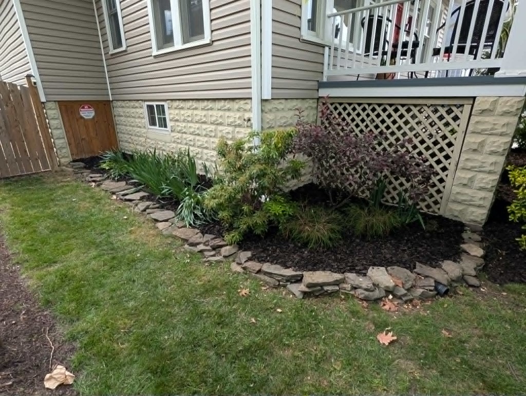 Mulched garden bed with natural stone edging along a residential foundation