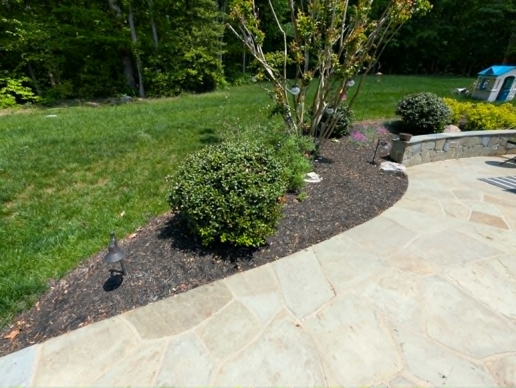 Flagstone patio with mulched garden bed, boxwood, and stone retaining wall