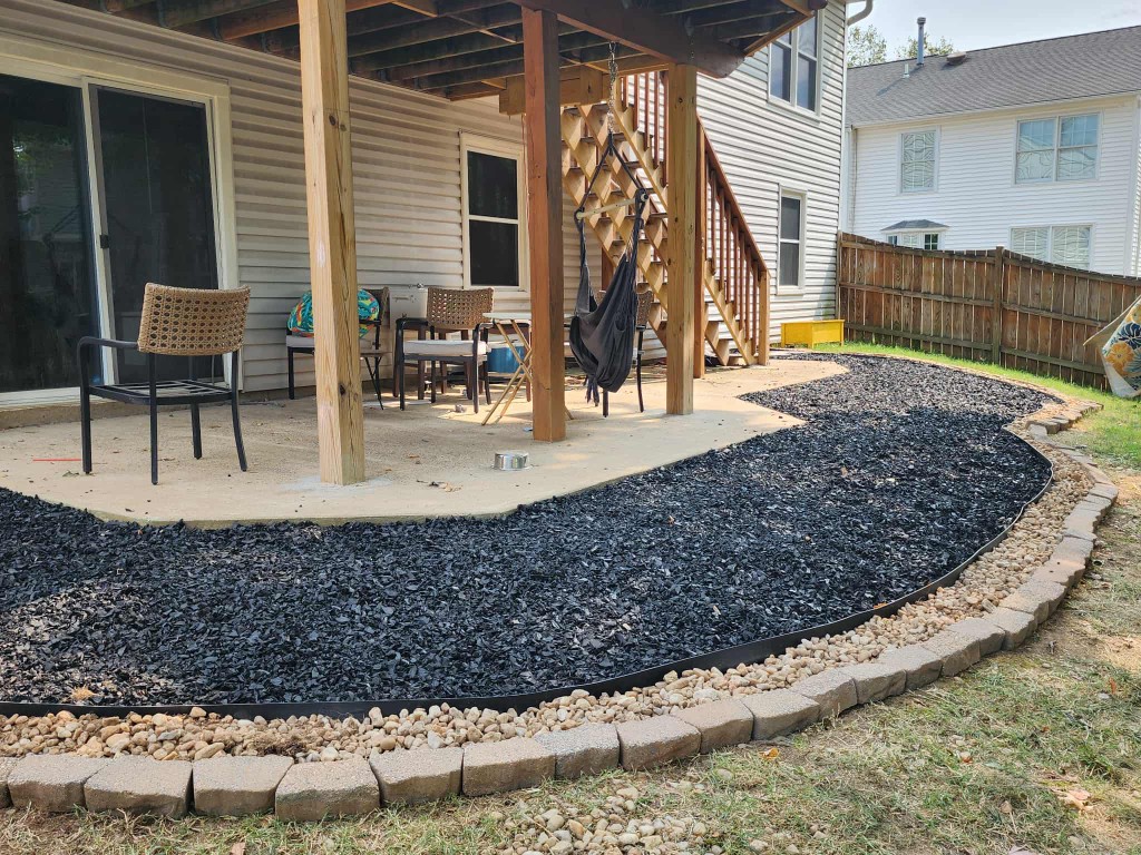Curved mulch bed with river rock border and stone pavers along a patio and deck