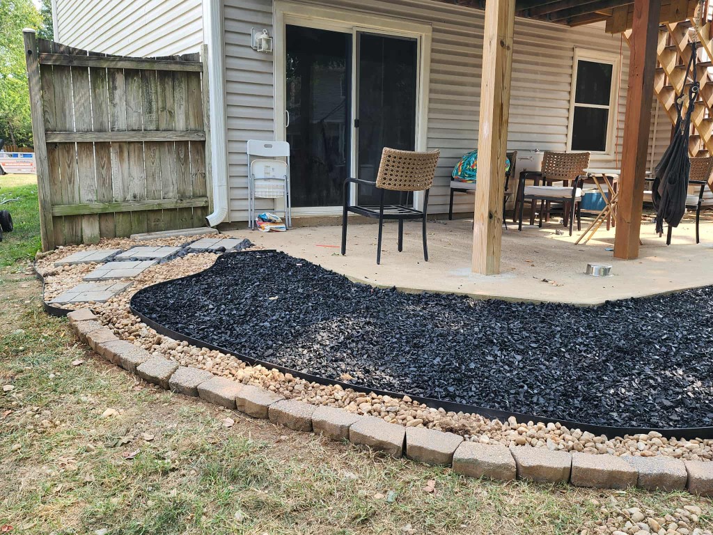 Patio landscaping bed with black mulch, river stones, pavers, and stepping stones