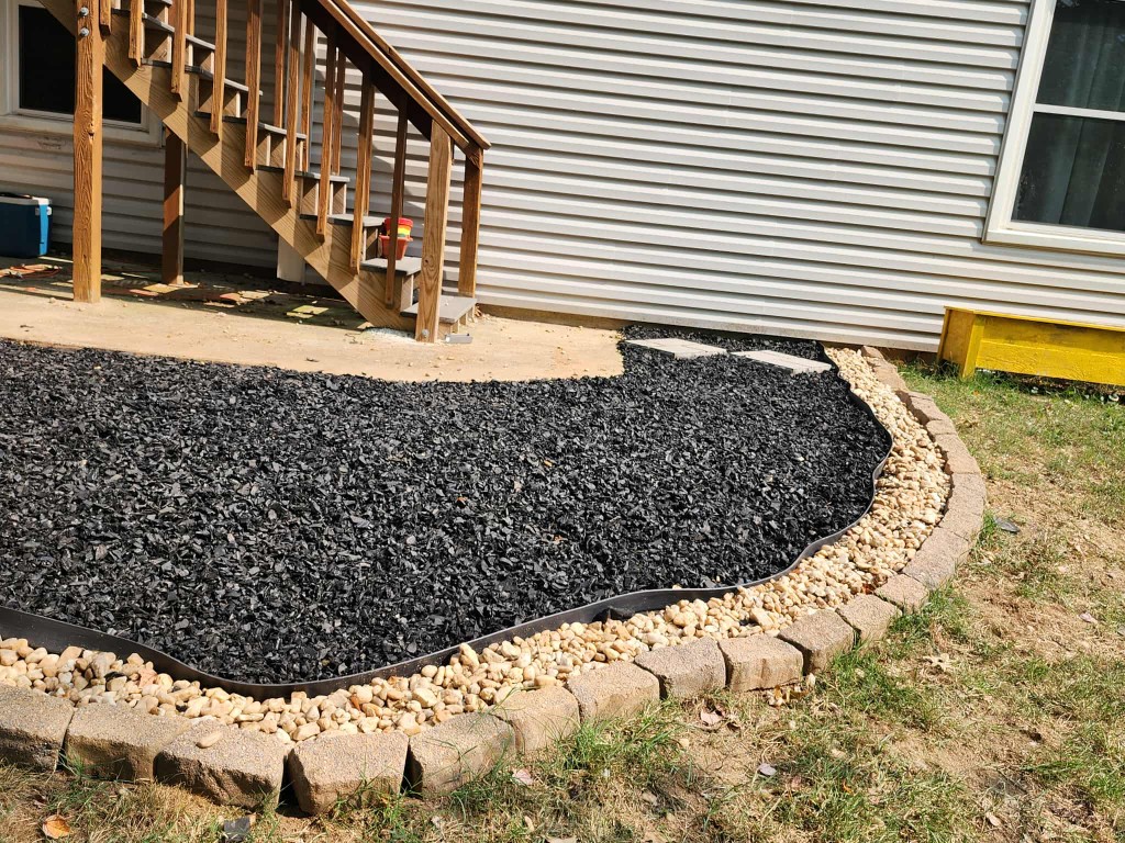 Finished curved garden bed with black mulch, pebble border, and stone block edging