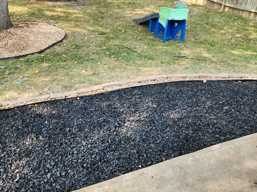 Close-up of layered landscape edging with black mulch, river rock, and paver border
