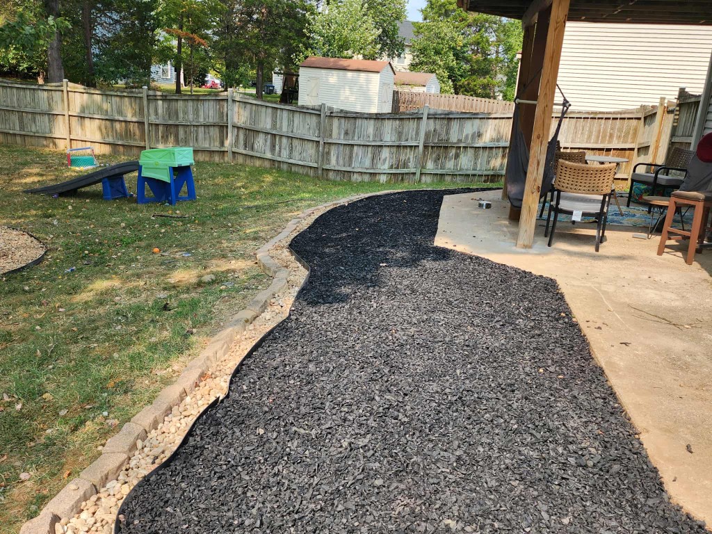 Wide backyard landscape bed with black mulch, stone border, and patio transition