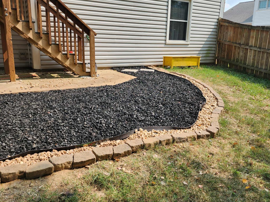Side-yard landscape bed with black mulch, river rock, pavers, and stepping stones