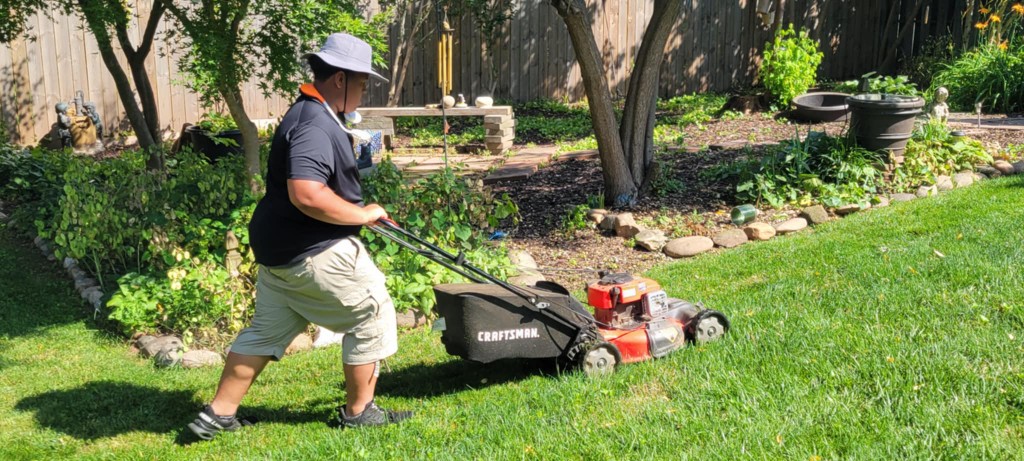 Londyn mowing a backyard with garden beds and clean striping