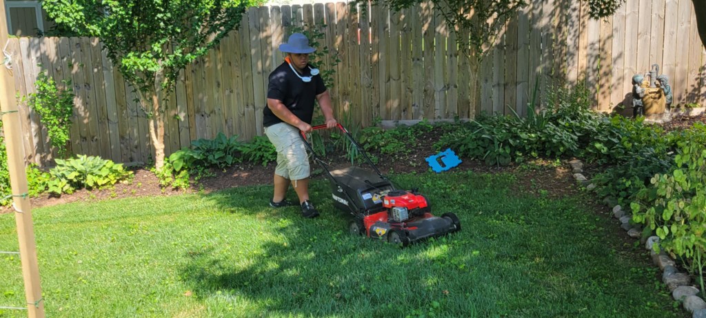 Londyn mowing a backyard lawn near a blue deck