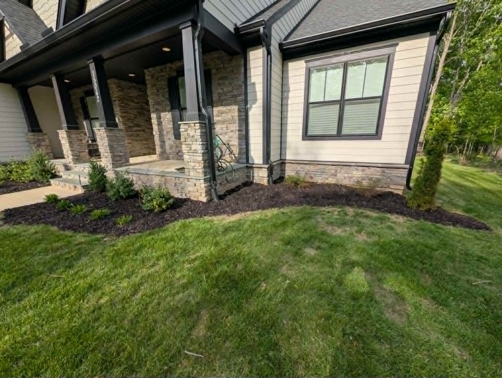 Curved foundation mulch bed with shrubs and stone porch columns